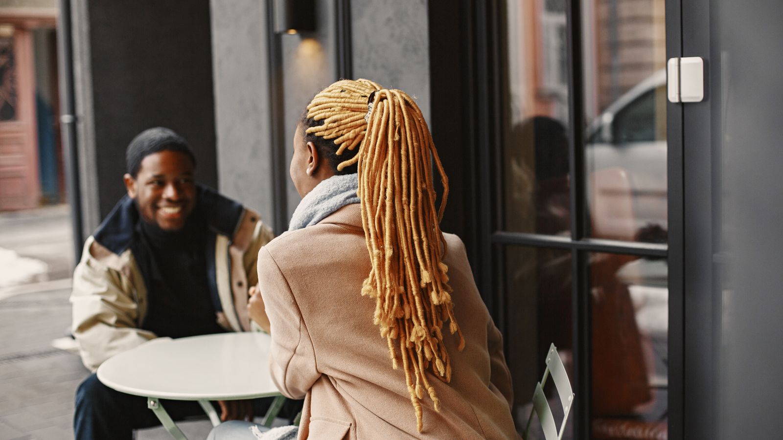 Two people talking at an outdoor café table in coats