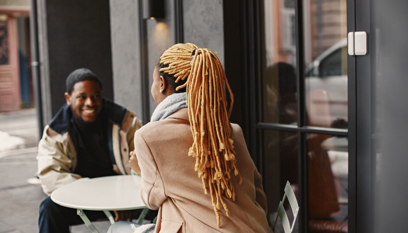 Two people sitting at an outdoor cafe table in conversation on a cool day