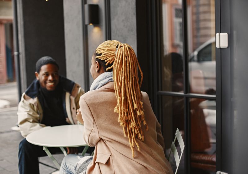 Two people sitting at an outdoor cafe table in conversation on a cool day