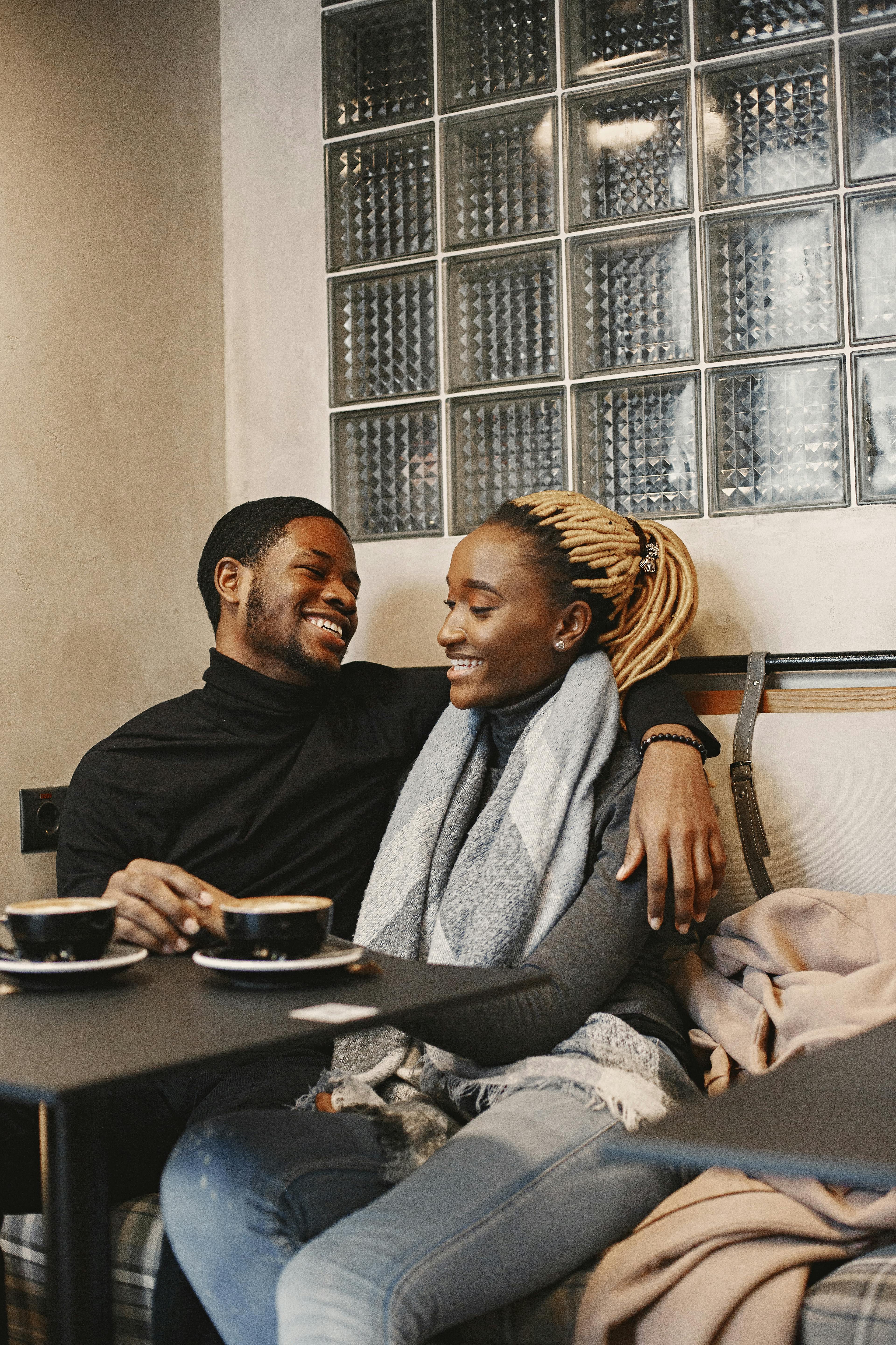 A happy couple sitting closely in a cozy coffee shop, enjoying drinks and each other's company.