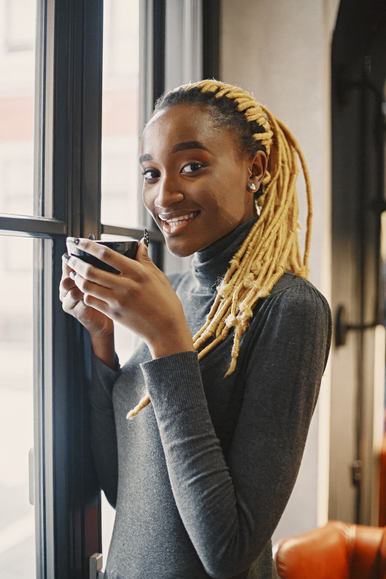 Woman wearing a fine-gauge gray turtleneck sweater by a window