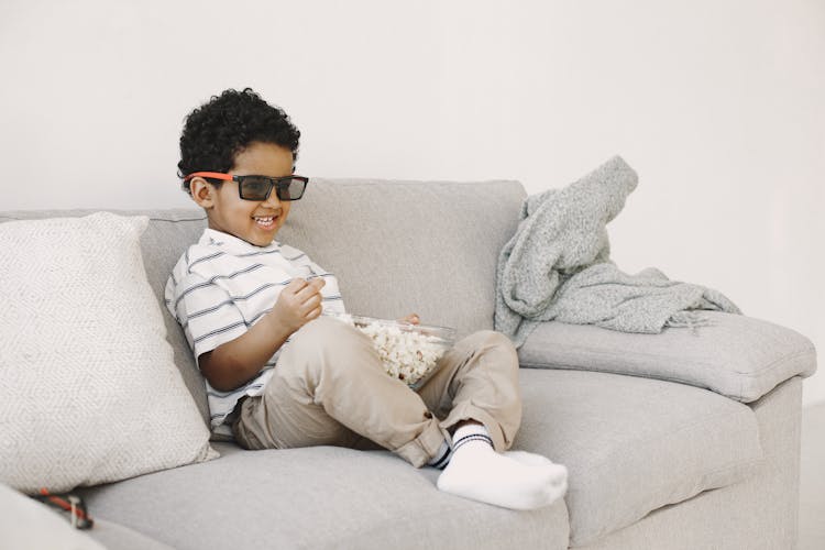 A Boy Eating Popcorn While Sitting On The Couch