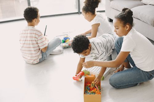 Free Four children engaged in creative play with toys on the living room floor, fostering imagination and teamwork. Stock Photo