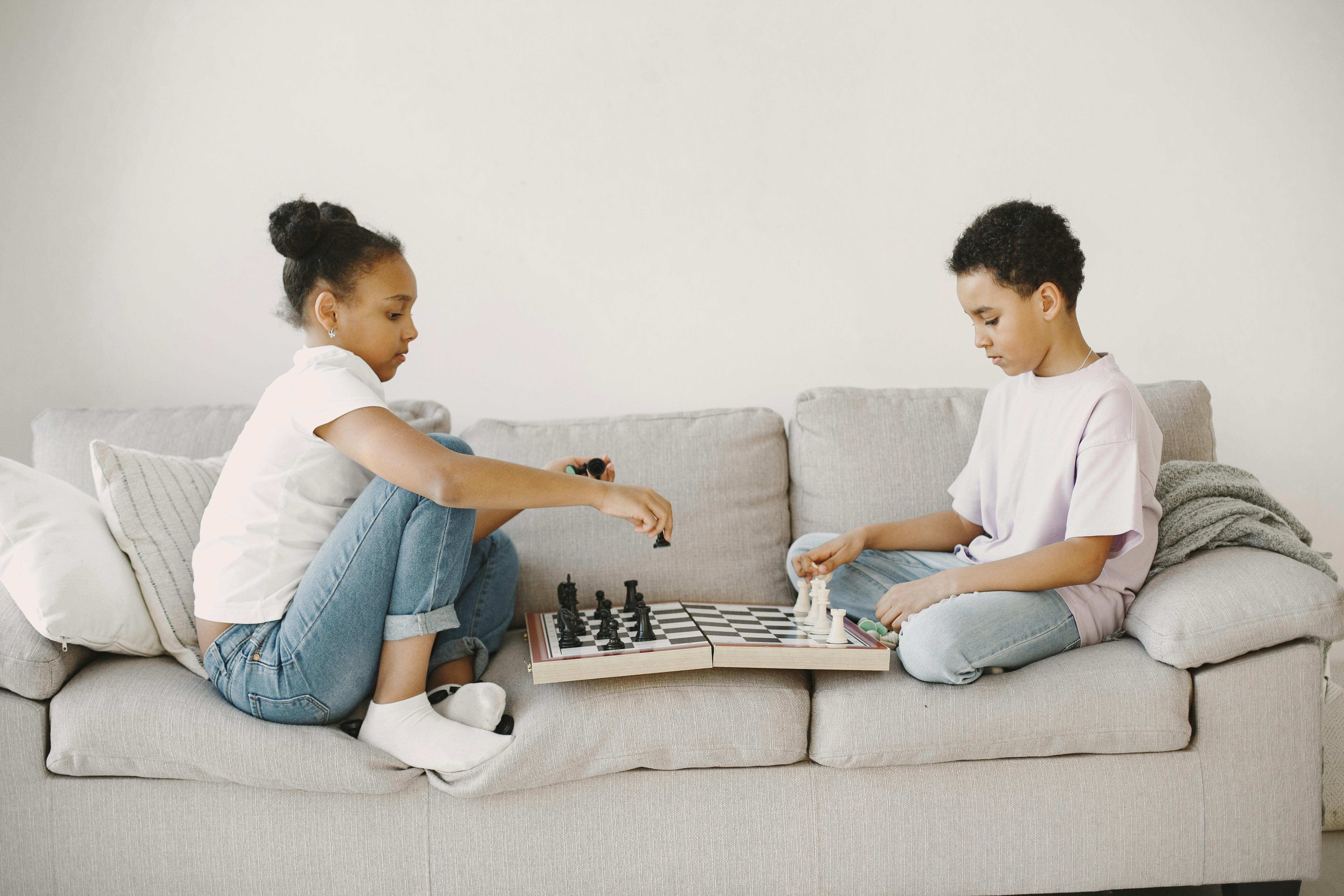 a girl and a boy playing chess on the sofa