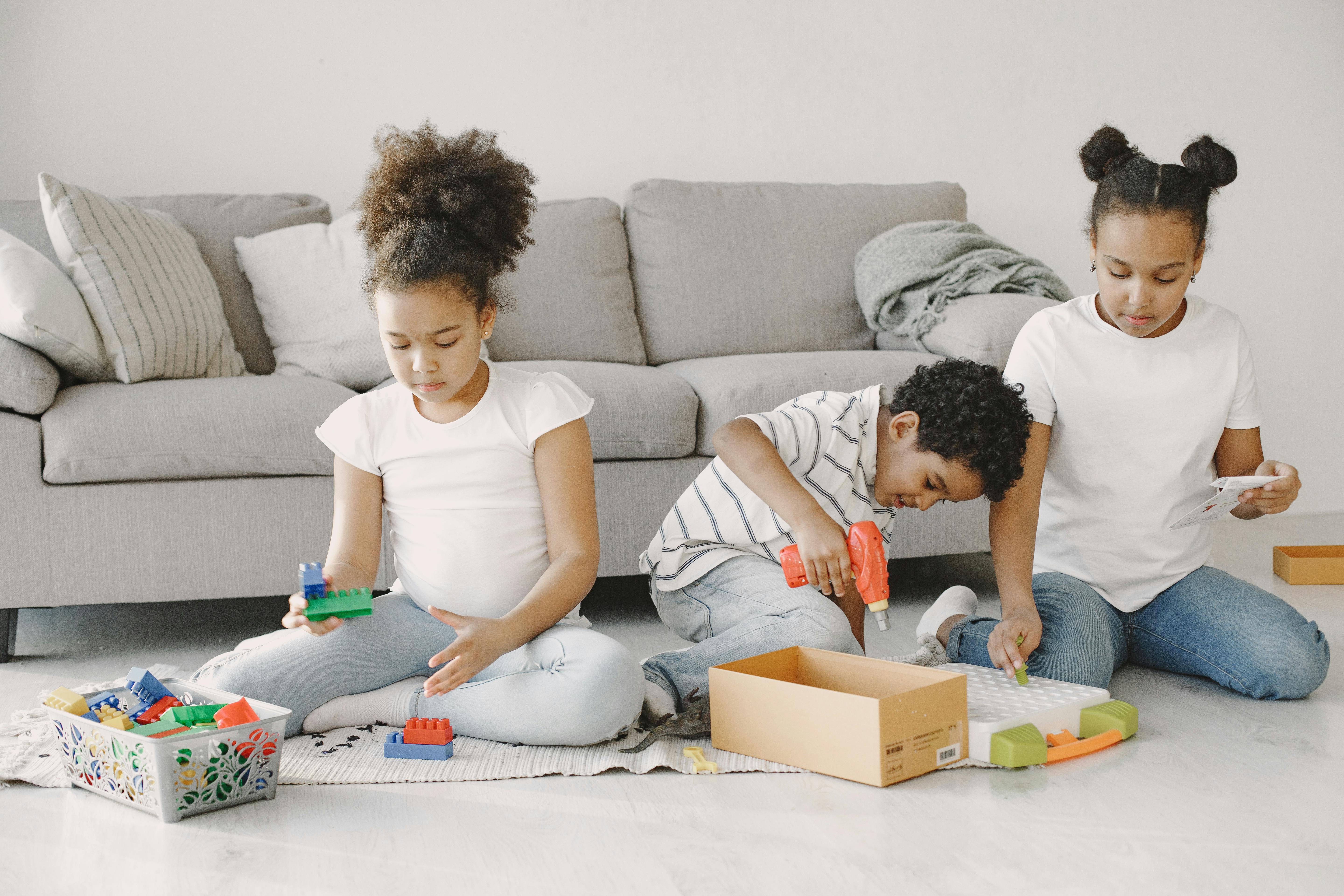 Three children engaged in creative play with educational toys, sitting on the floor in a cozy living room setting.