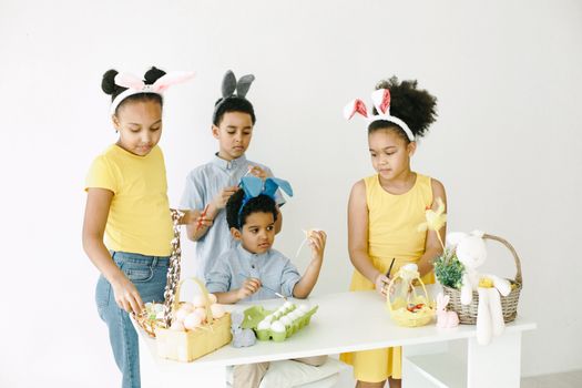 A group of children in bunny ears decorating and crafting Easter eggs indoors.