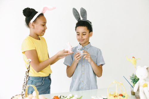 Free Boy and girl with bunny ears engage in Easter fun, holding bunny figurines indoors. Stock Photo