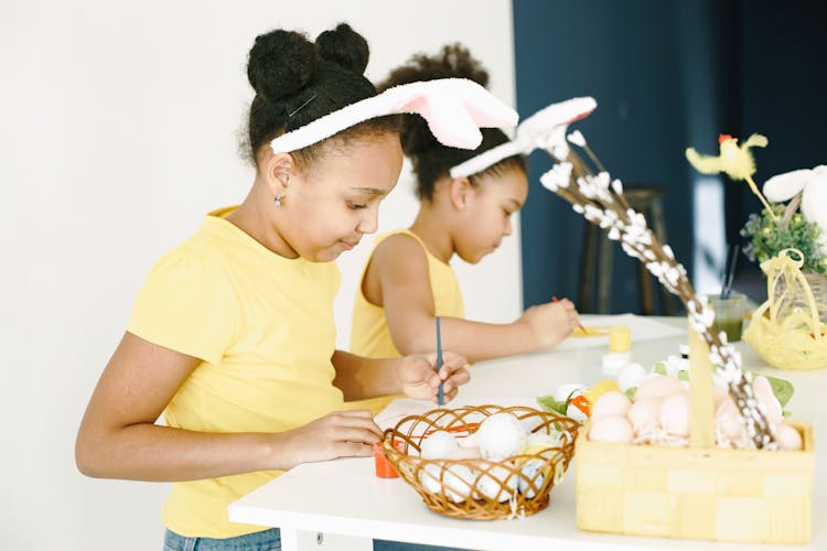 Twin Girls In Yellow T-Shirts And Bunny Ears Painting Easter Eggs