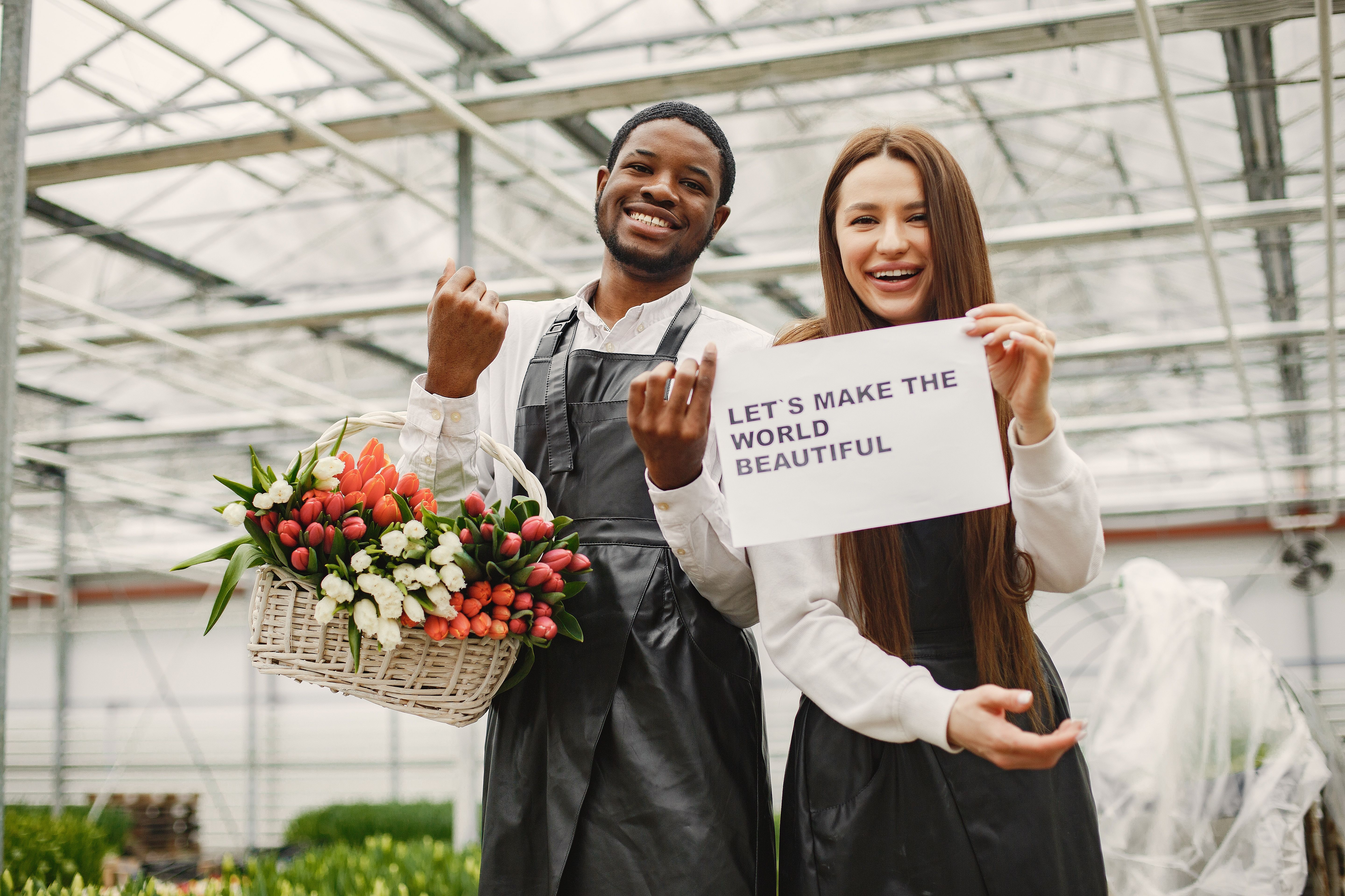 A joyful duo showcasing vibrant flowers in a greenhouse, spreading positivity.