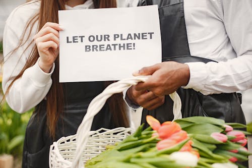 Close-up of Man and Woman Holding a Paper Sheet with Let Our Planet Breathe Sign on It and a Basket Full of Tulips 