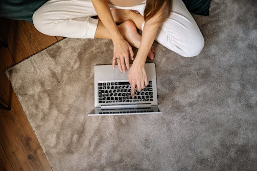 Overhead view of a woman using a laptop on a carpeted floor, relaxing in a home setting.