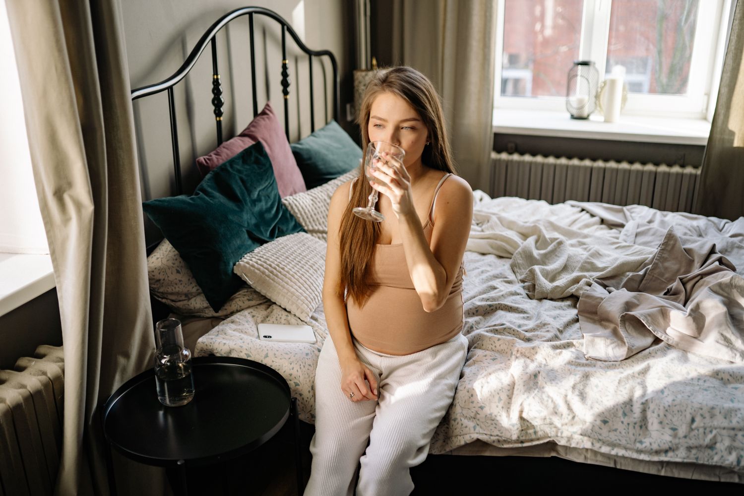 Femme enceinte assise dans une chambre calme avec un verre d’eau