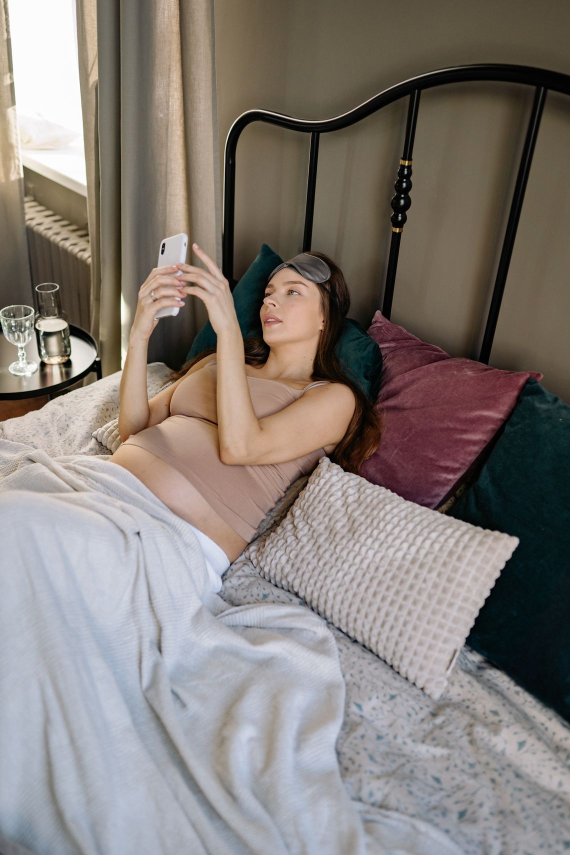 Pregnant woman using a smartphone while relaxing on a bed