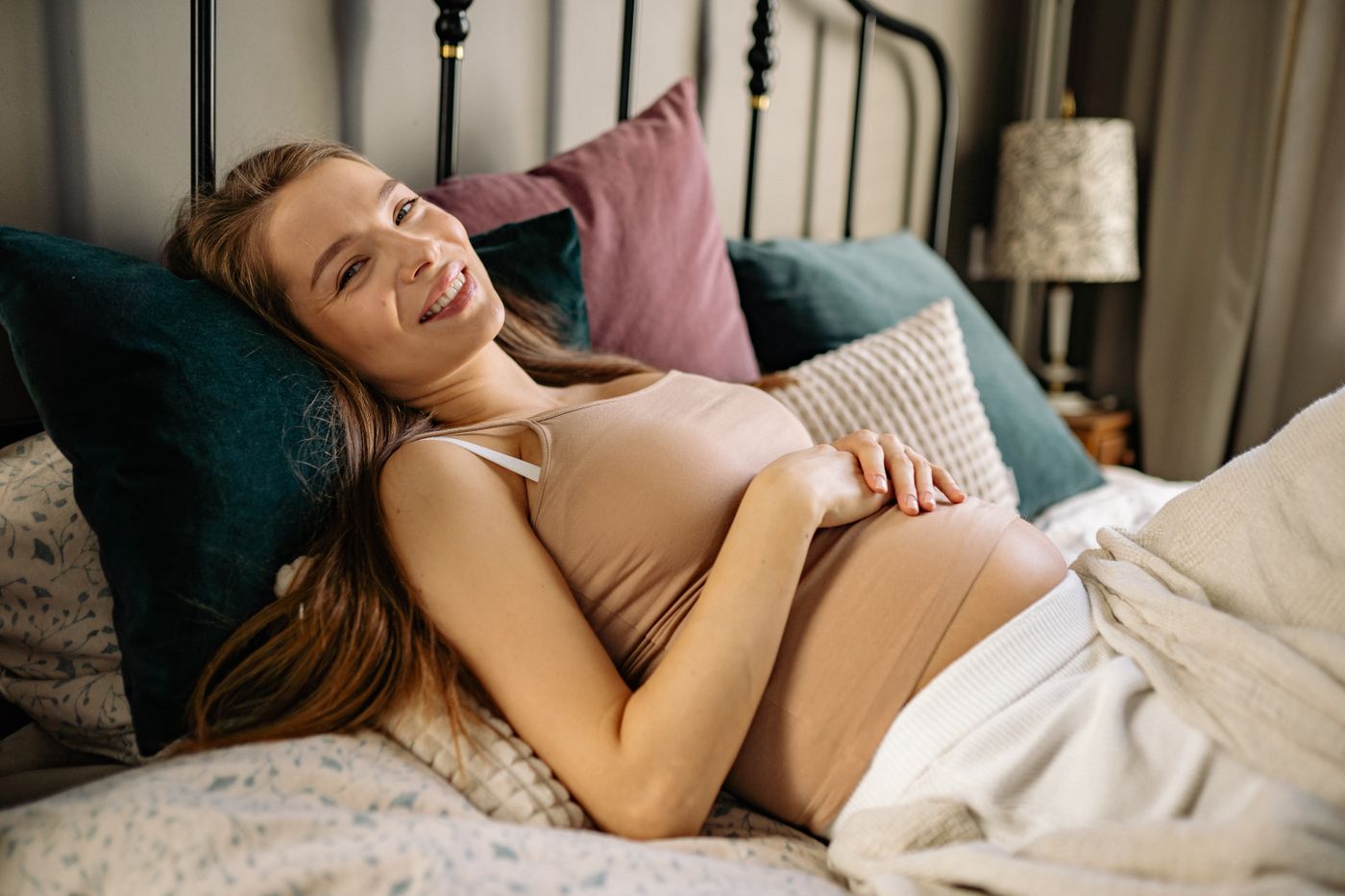 Future maman souriante confortablement installée dans une chambre naturelle