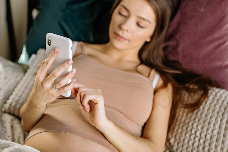 Woman Using Her Iphone While Lying On Bed 