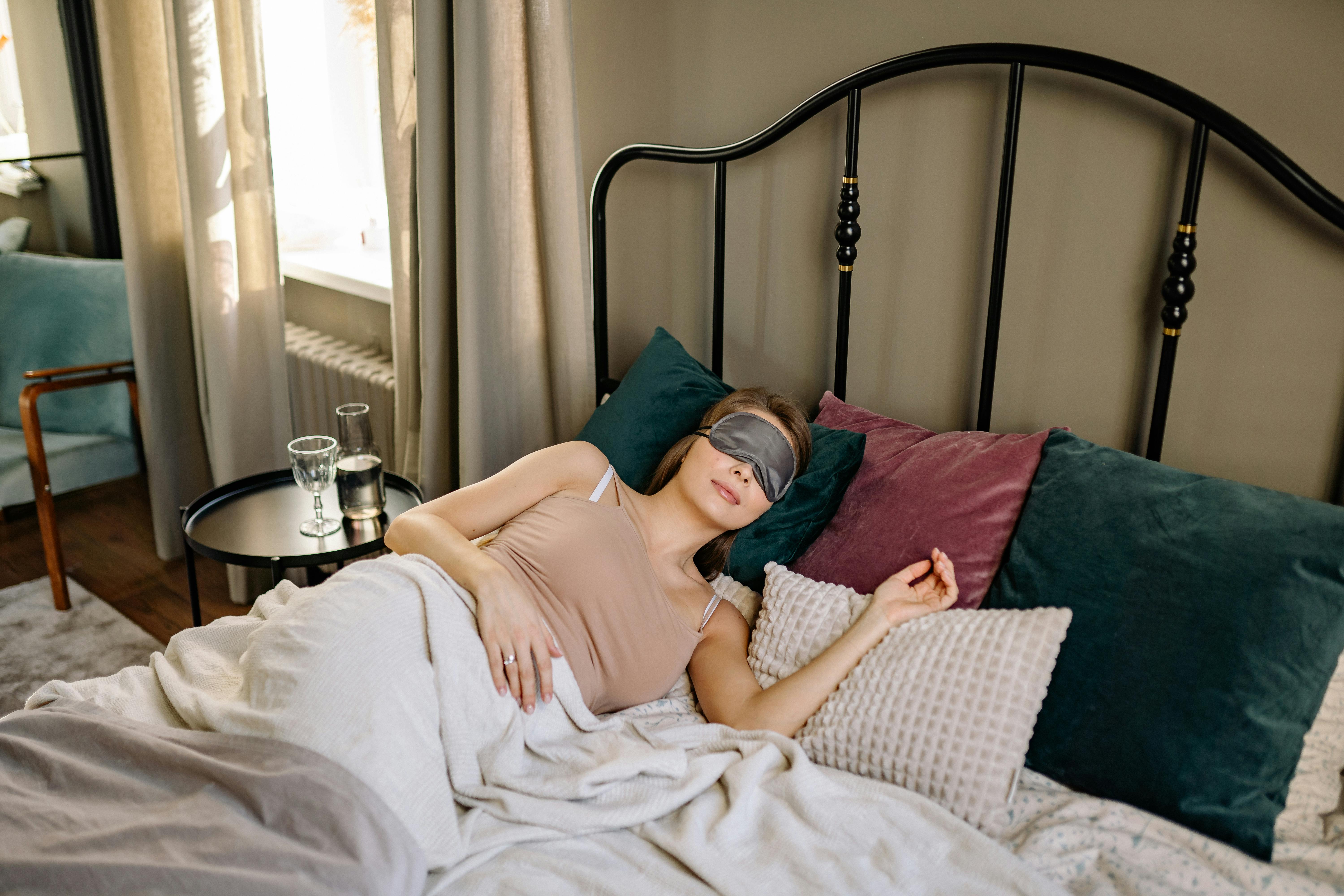 Woman sleeping comfortably in bed with an eye mask and pillows.