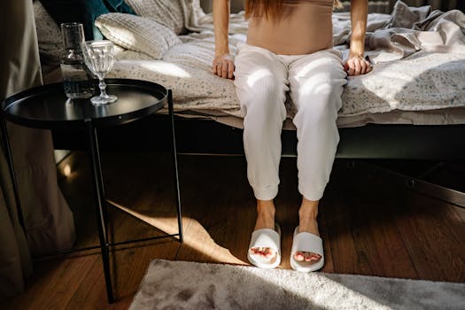 Person relaxing in a cozy bedroom setting with soft lighting and casual attire.