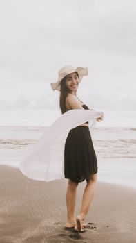 Woman in summer dress and hat smiling on the beach in Bali, Indonesia.