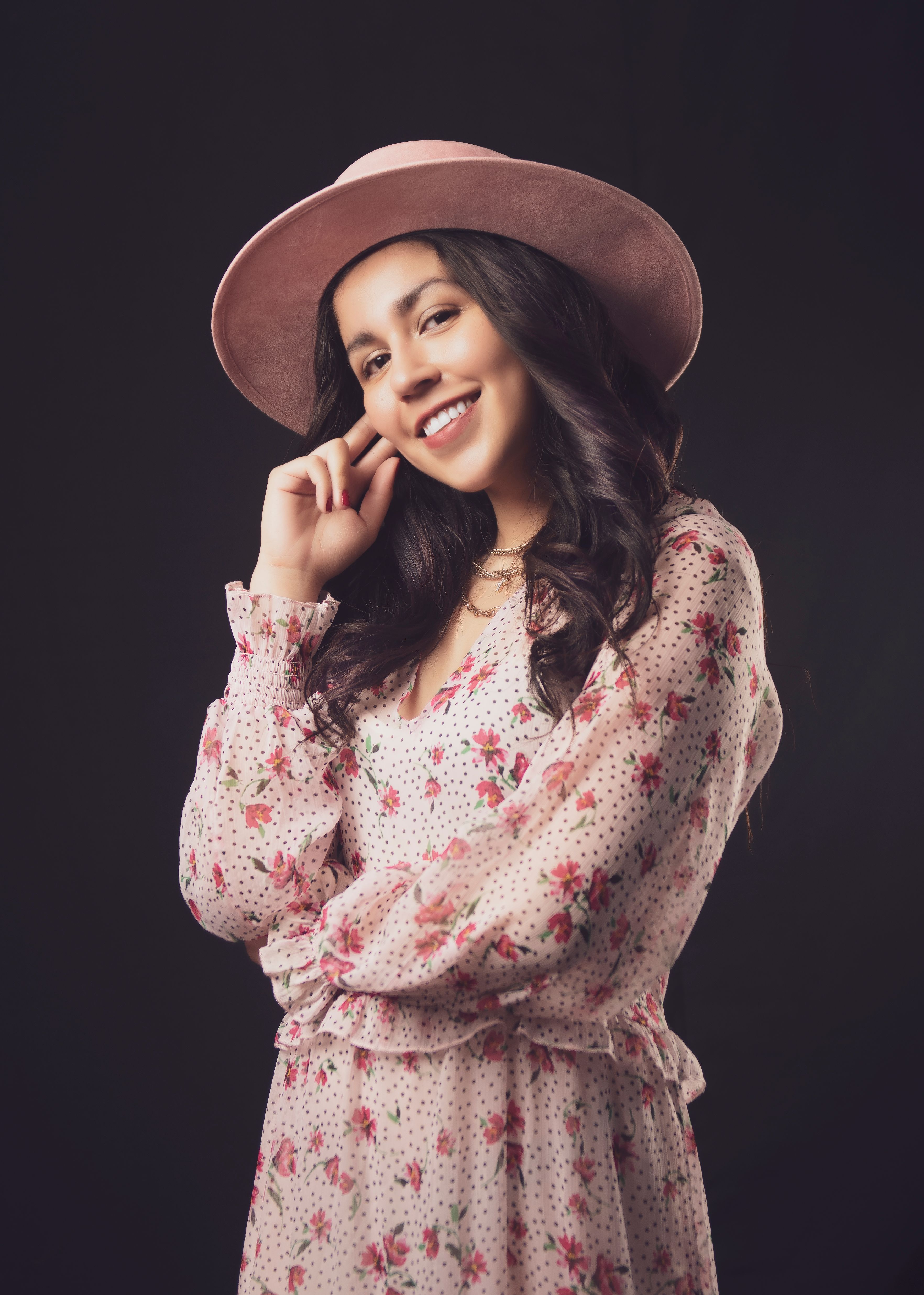 Smiling woman in floral dress and pink hat posing confidently