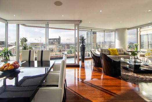 Bright modern living space with glass walls and elegant furniture overlooking cityscape.