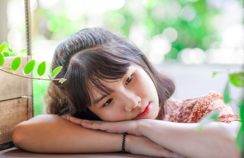 Free A young woman with black hair daydreaming, leaning on a wooden table with greenery around. Stock Photo