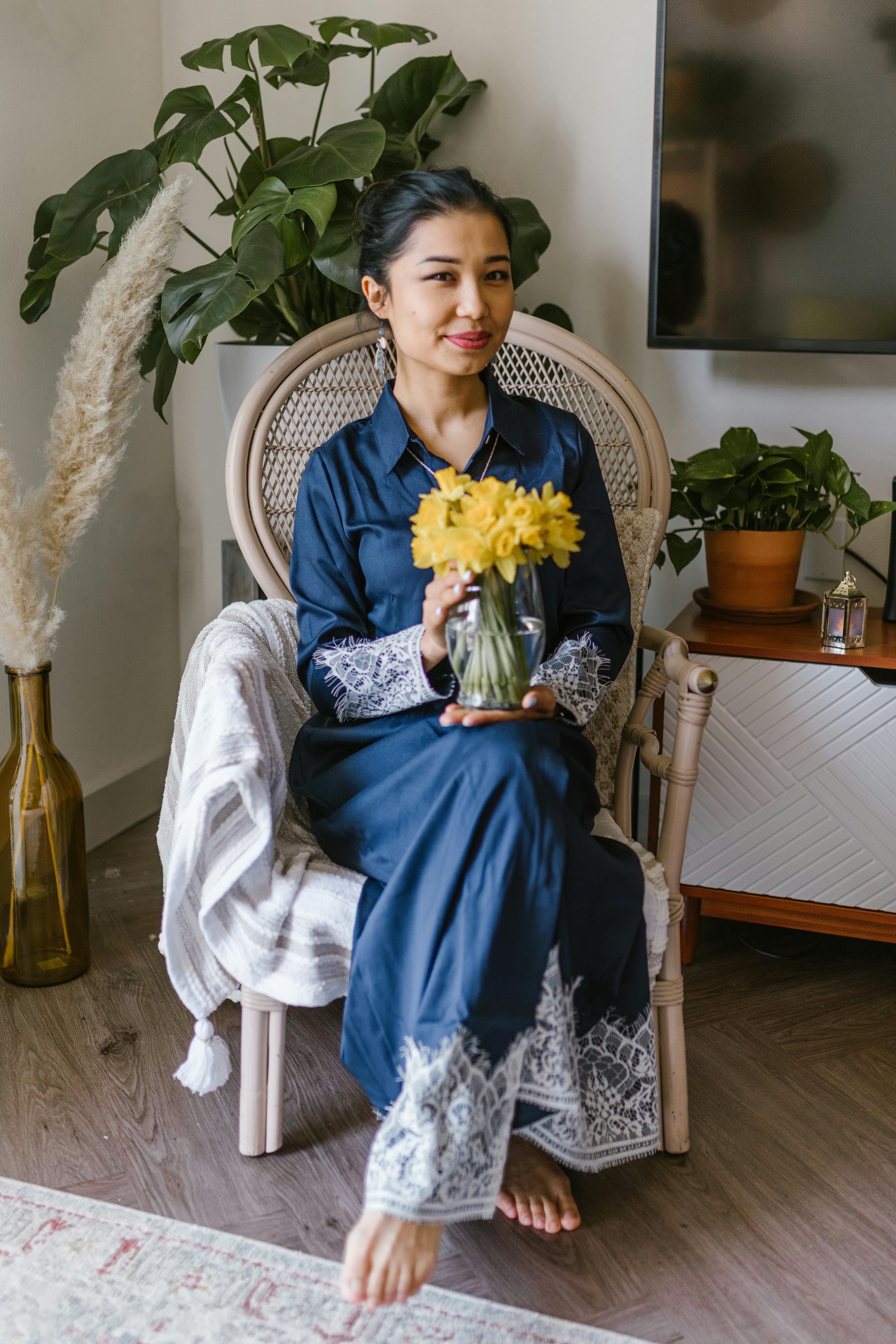 A woman seated indoors holding yellow flowers, celebrating Nowruz in a traditional setting.
