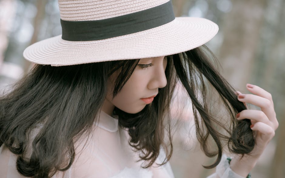 Elegant young woman in hat posing outdoors with a serene expression.