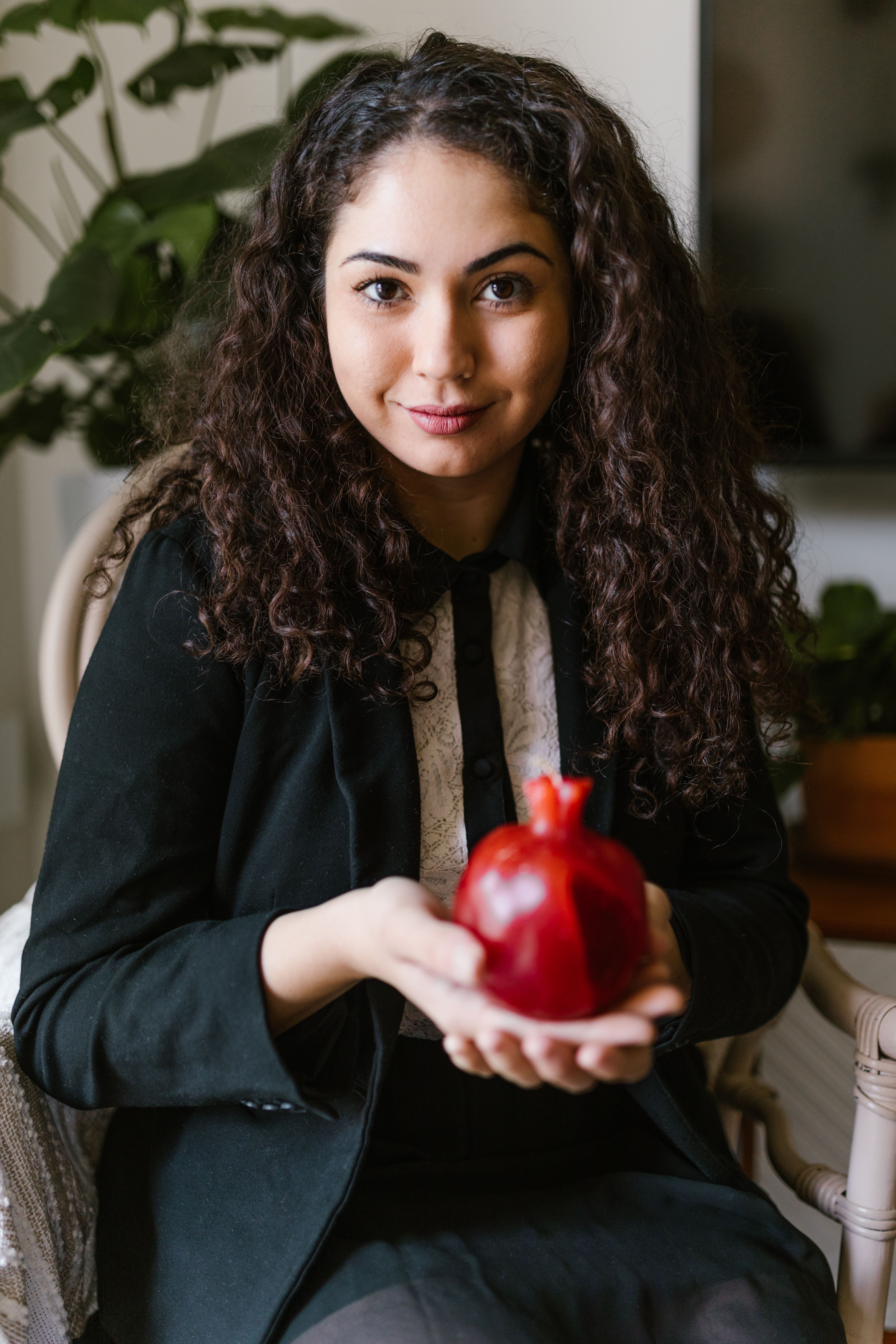 Young woman indoors holding a pomegranate, celebrating Nowruz, symbolizing new beginnings and prosperity.