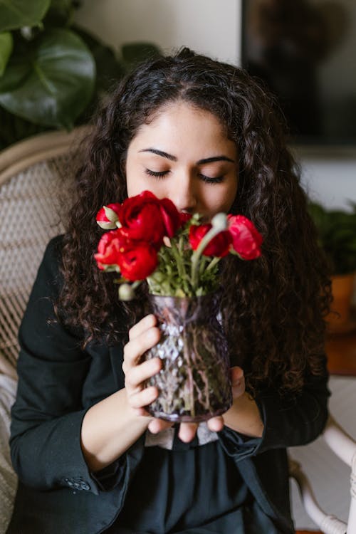 Woman Smelling Red Flowers In A Vase