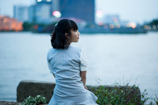黄昏时分，一个女人坐在河边，背景是城市的灯光