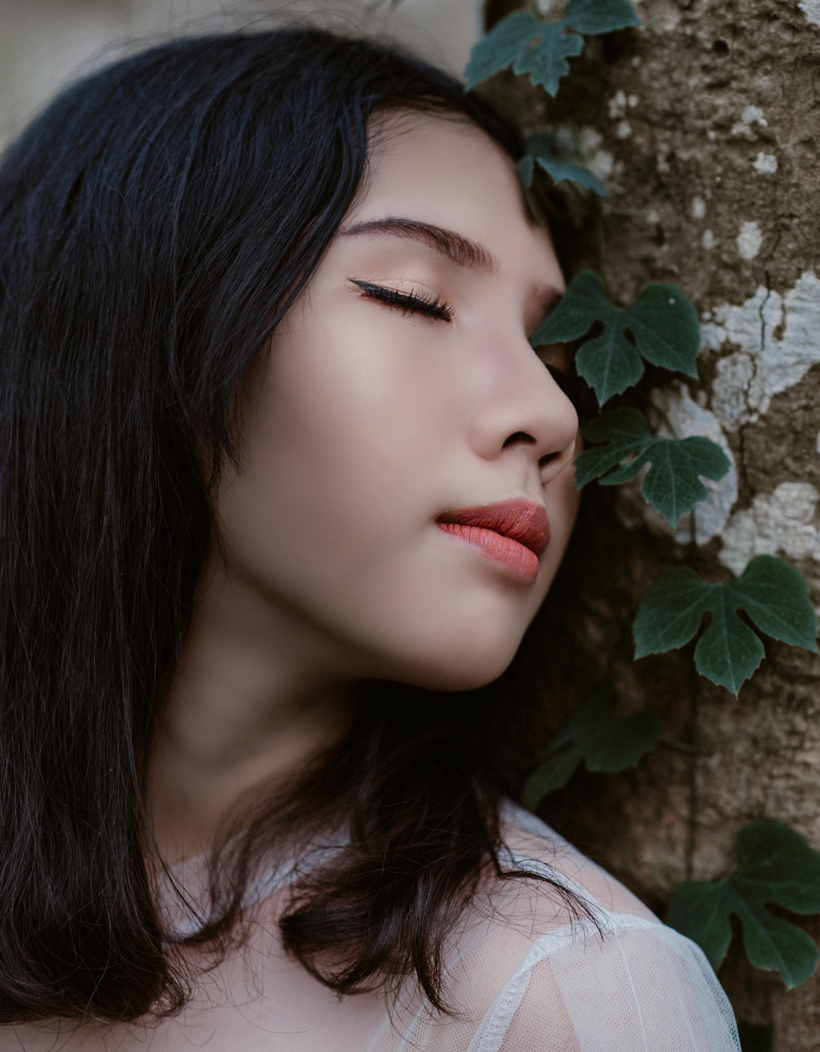 woman closing her eyes beside green vine plant