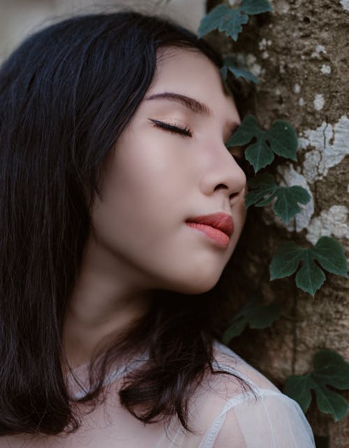 Free Woman Closing Her Eyes Beside Green Vine Plant Stock Photo