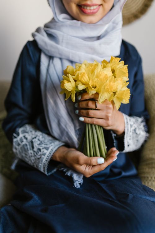 Free Smiling woman in headscarf holds vibrant yellow daffodils, embodying warmth and spring indoors. Stock Photo