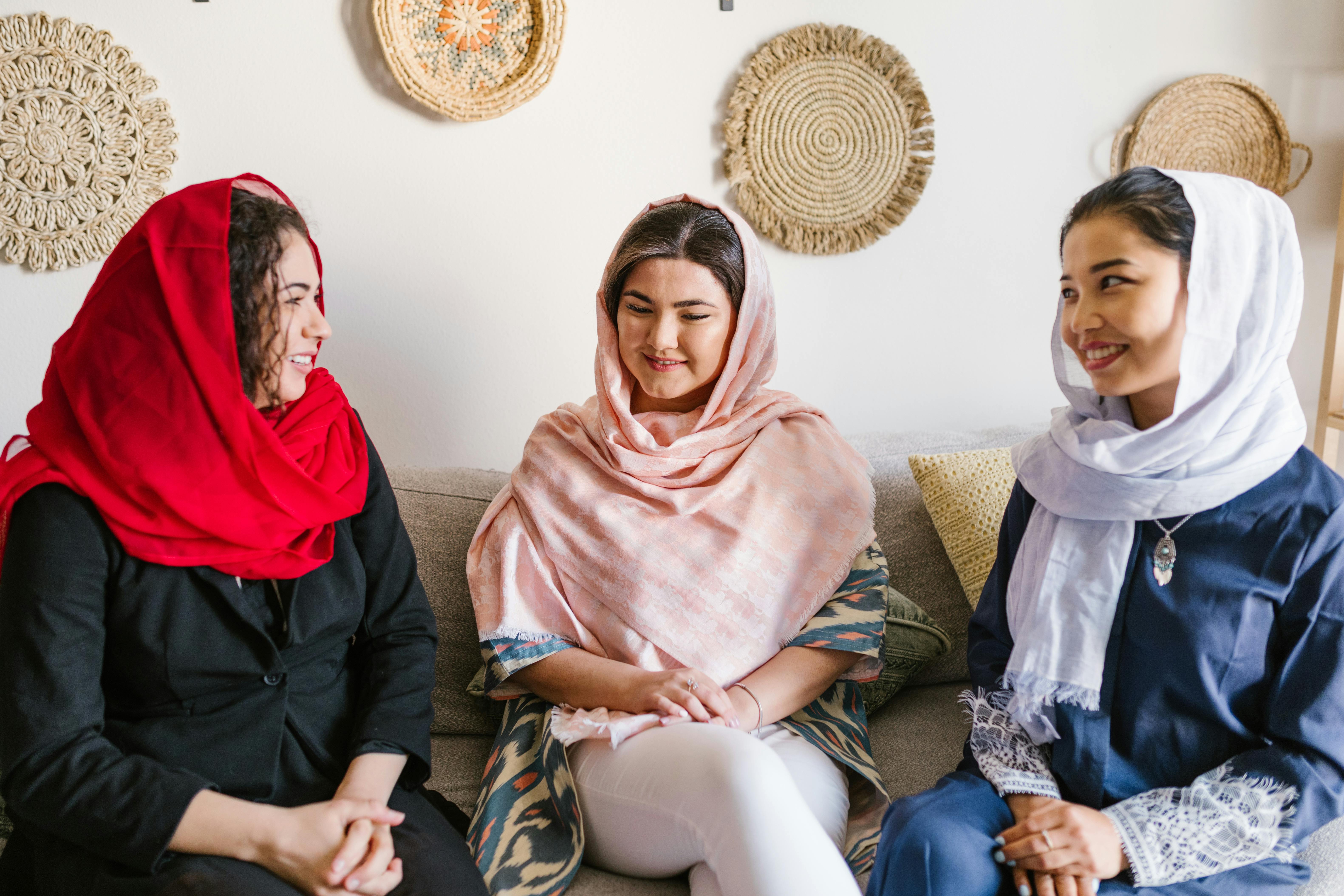 Three women in traditional attire sharing smiles and togetherness indoors during Nowruz.