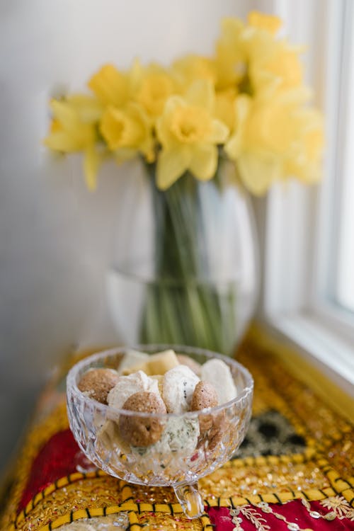 Glass Bowl Of Food And Vase With Yellow Flowers On Table