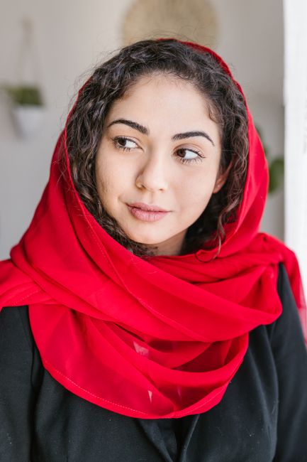 A woman wearing a vibrant red scarf looks serene in a softly lit indoor setting.