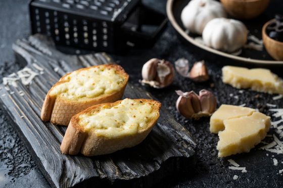 Two toasted baguette halves topped with bubbling melted garlic cheese on a dark wooden board
