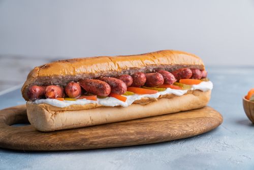 Free Deliciously presented hotdog with toppings on a wooden board, perfect for American food enthusiasts. Stock Photo