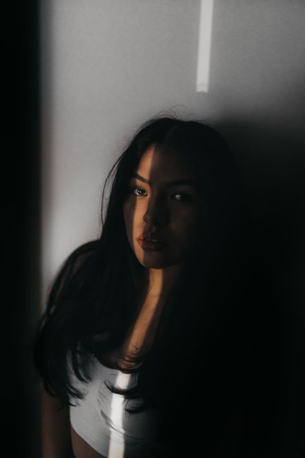 High angle of young female with dark long dark hair standing near wall and shadow on face