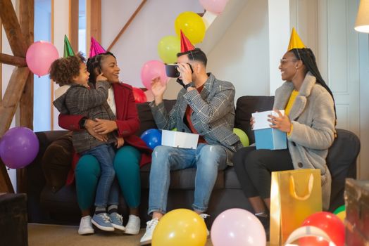 A family celebrates with balloons and VR headset, capturing joyful moments together indoors.