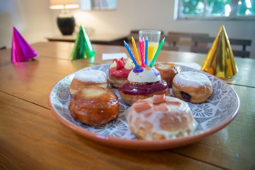 Plate of assorted donuts with birthday candles and party hats on a wooden table.