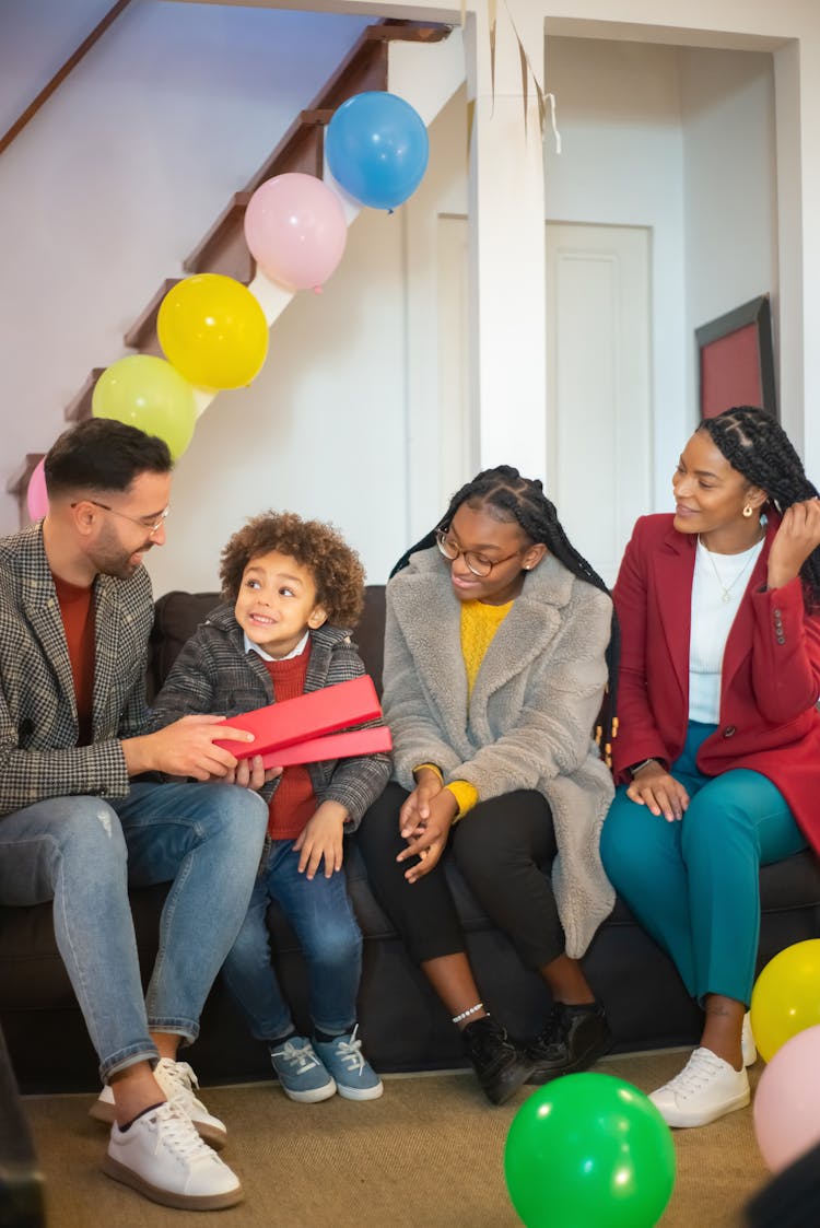 A Man Holding A Box Sitting On A Couch With His Family