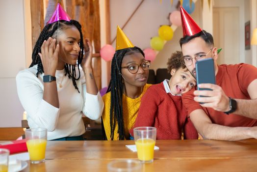 Family celebrating with birthday hats, taking a cheerful selfie indoors.