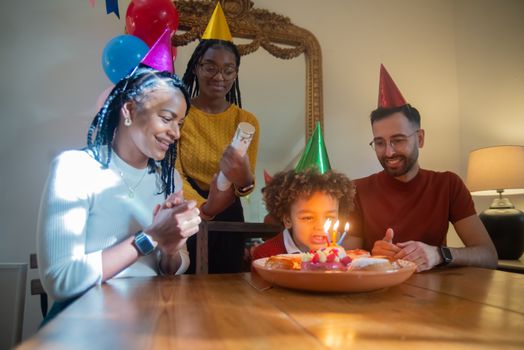 A diverse family celebrates a child's birthday with cake, hats, and smiles indoors.