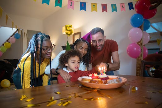 Joyful family celebrating a child's 5th birthday with cake and candles indoors.
