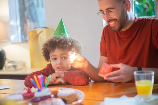 A child and adult celebrating a birthday indoors with cake and candles.