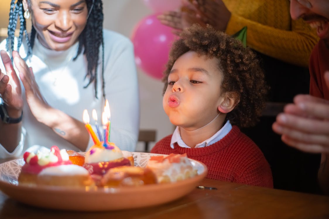 Free A Boy Wearing Party Hat Blowing the Lighted Candles Stock Photo