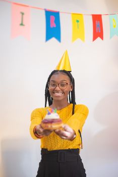 Young woman celebrating birthday with a cupcake and colorful decor indoors.