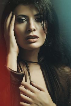 Charming young female model with bright makeup in stylish outfit touching face in dark studio