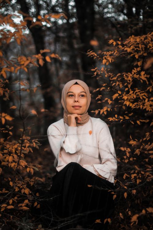 Free Thoughtful woman in hijab sitting amidst autumn foliage in forest Stock Photo